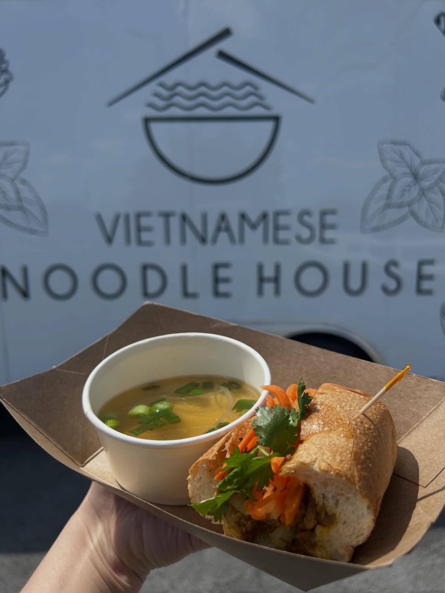 Banh mi and a cup of broth held in front of the food truck